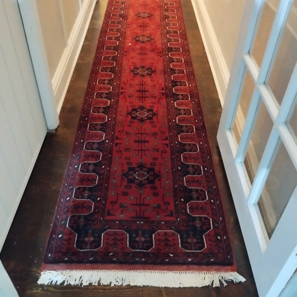 Long red Afghan Khal Muhammadi runner on a wooden floor in a hallway