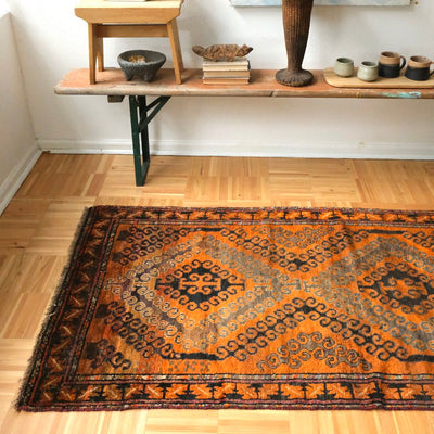 Decorative rug on a wooden floor with a shelf and artwork in the background