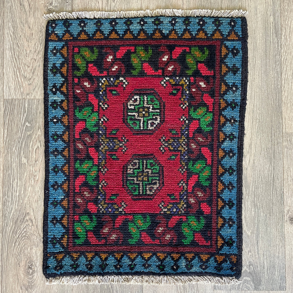 Small Afghan Aqcha handmade wool doormat featuring traditional red and navy elephant foot Mori gul patterns, styled on a light oak wood floor.