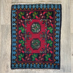 Small Afghan Aqcha handmade wool doormat featuring traditional red and navy elephant foot Mori gul patterns, styled on a light oak wood floor.