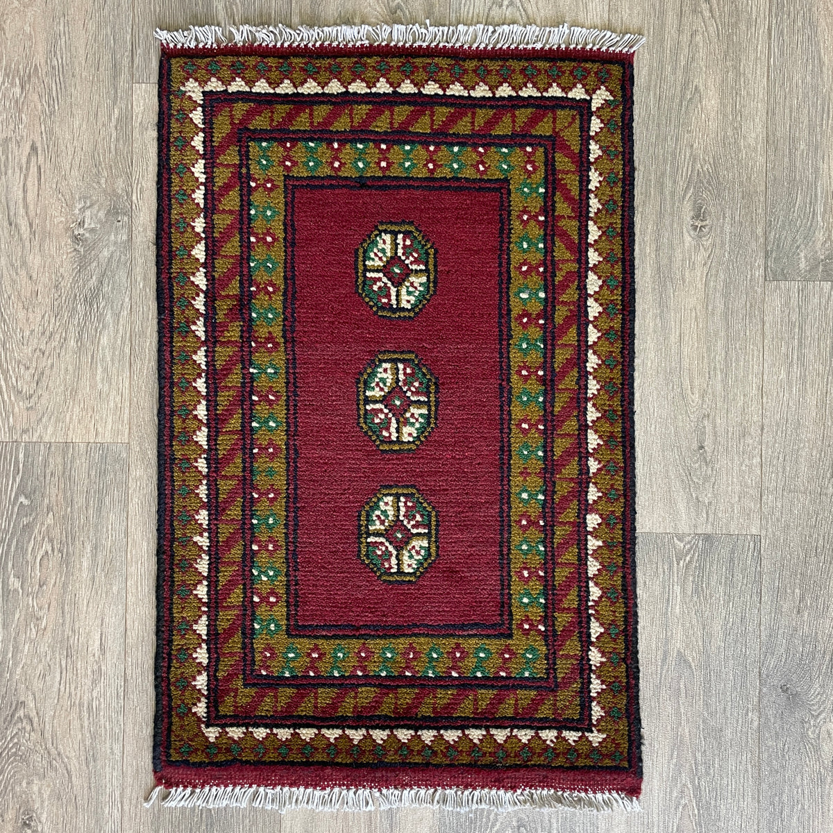 Small Afghan Aqcha handmade wool doormat featuring traditional red and navy elephant foot Mori gul patterns, styled on a light oak wood floor.