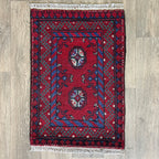Small Afghan Aqcha handmade wool doormat featuring traditional red and navy elephant foot Mori gul patterns, styled on a light oak wood floor.