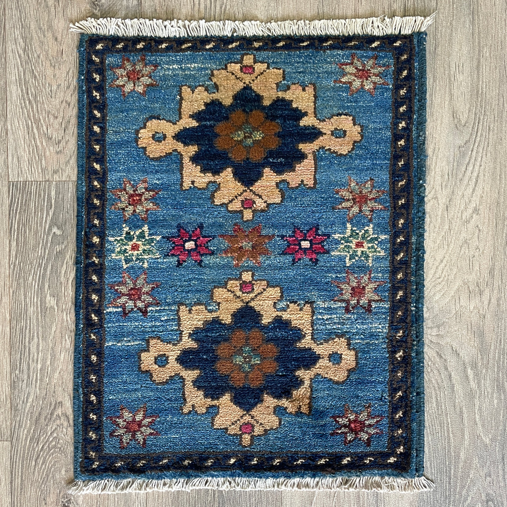 Small Afghan Sultanabad handmade wool doormat featuring an oversized floral palmette and vine design in muted blue, styled on a light oak wood floor.