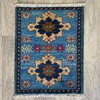 Small Afghan Sultanabad handmade wool doormat featuring an oversized floral palmette and vine design in muted blue, styled on a light oak wood floor.