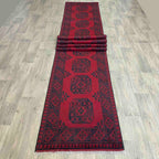 Traditional red Afghan Aqcha wool runner rug featuring a repeating elephant foot Mori gul pattern, displayed on a light oak wood floor.