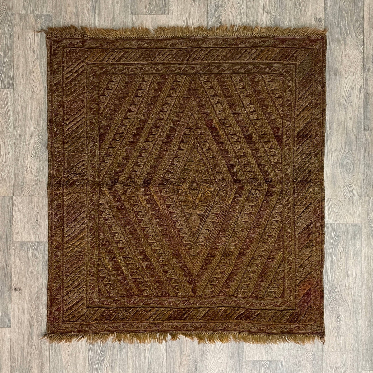 Handmade Afghan brown Mushwani tribal rug featuring a unique combination of flat-weave kilim and raised wool pile geometric diamond patterns, displayed on a light oak wood floor.