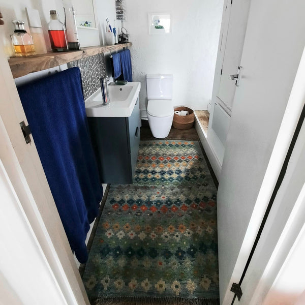 Bathroom with an Afghan kilim rug, blue shower curtain, and white toilet.