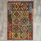 Handmade Afghan kilim flat-weave wool rug featuring bold geometric tribal patterns and braided fringes, laid flat on a light oak wood floor
