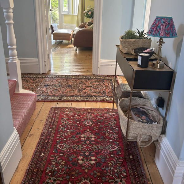 Narrow hallway with red Persian Hamadan rugs, wooden floor, and furniture.