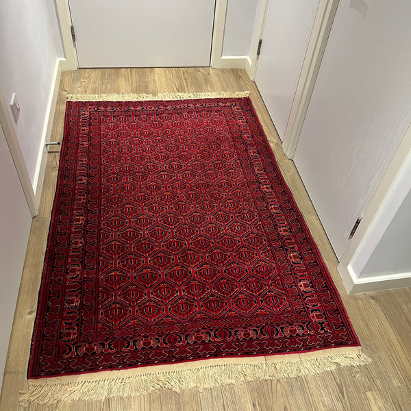 Red Afghan rug on a wooden floor with a white wall background