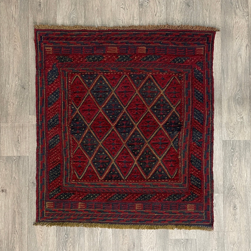 Handmade square Afghan brown Mushwani tribal rug featuring a unique combination of flat-weave kilim and raised wool pile geometric diamond patterns, displayed on a light oak wood floor.