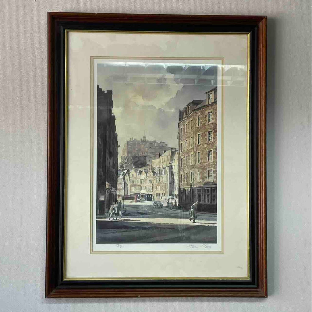 A framed art print depicting a vintage city street scene with historic buildings, mounted on a light gray wall.