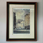 A framed art print depicting a vintage city street scene with historic buildings, mounted on a light gray wall.