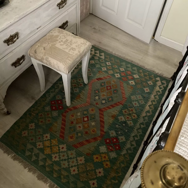 Small stool with a cushion on a patterned kilim rug in a room with a dresser and door.